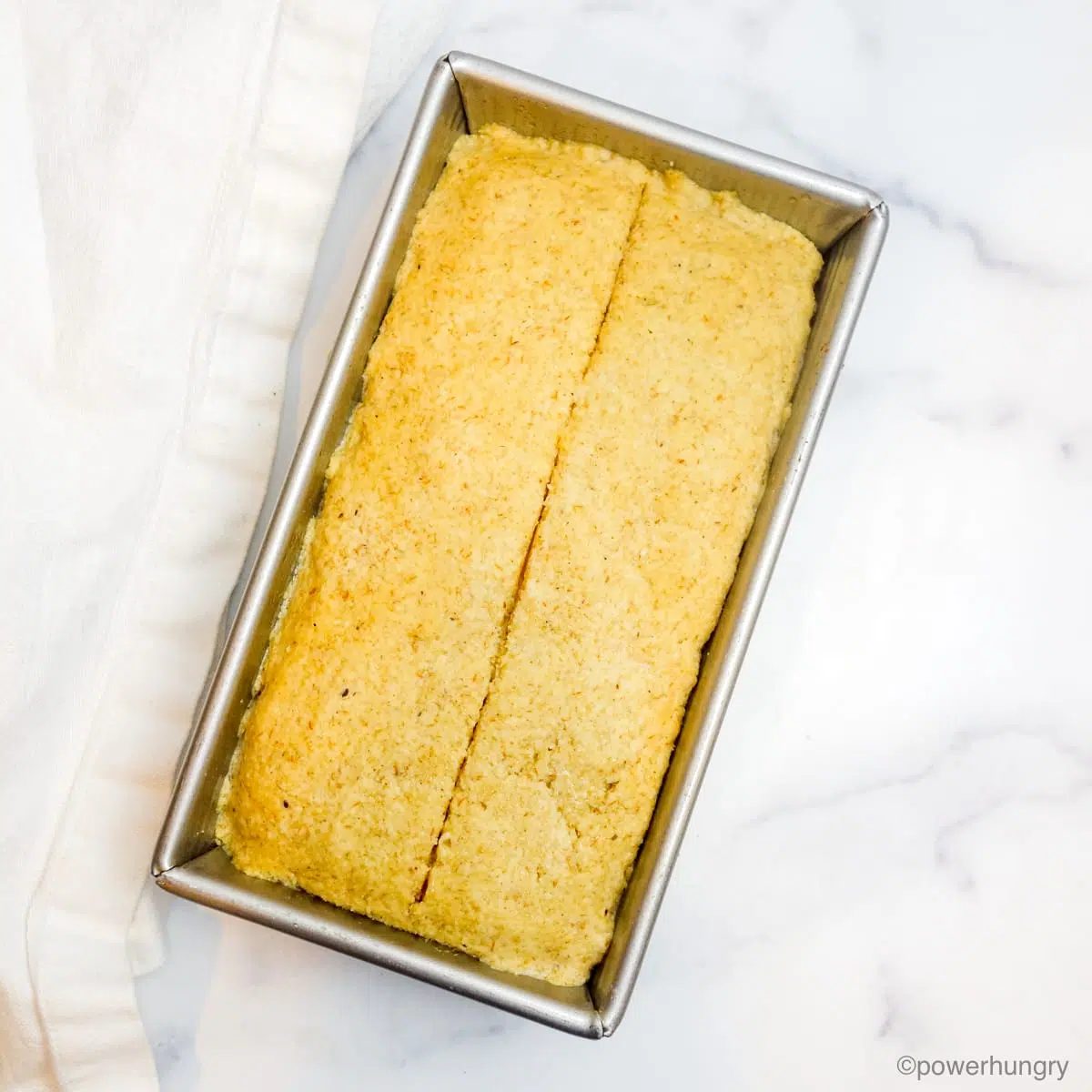 baked almond flour bread in a silver pan on a white marble background