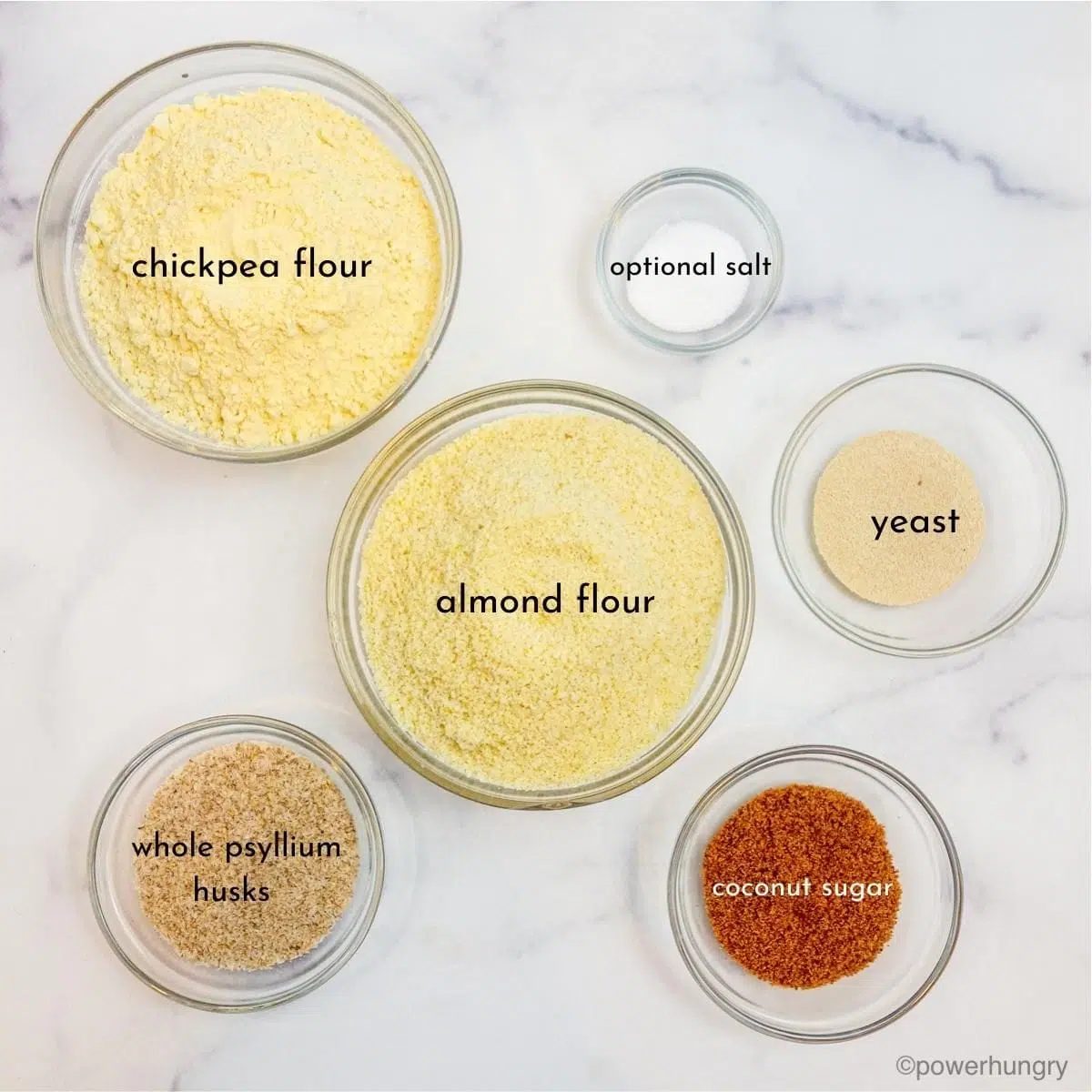 ingredients forvegan almond flour bread , all in small glass bowls, on a white marble surface
