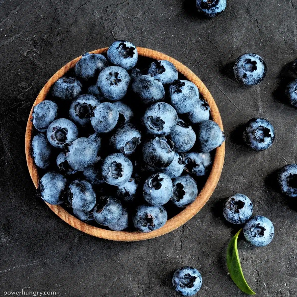 wooden bowl full of blueberries on a slate background