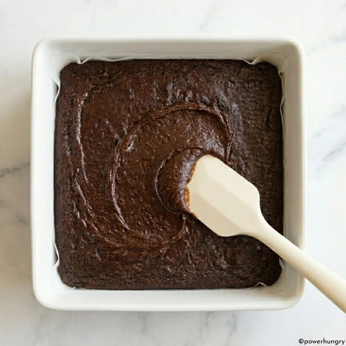 carob brownie batter getting spread in a square pan.