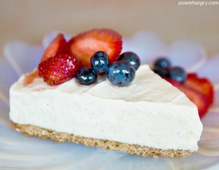 a slice of vegan cheesecake, topped with berries, on a lilac plate