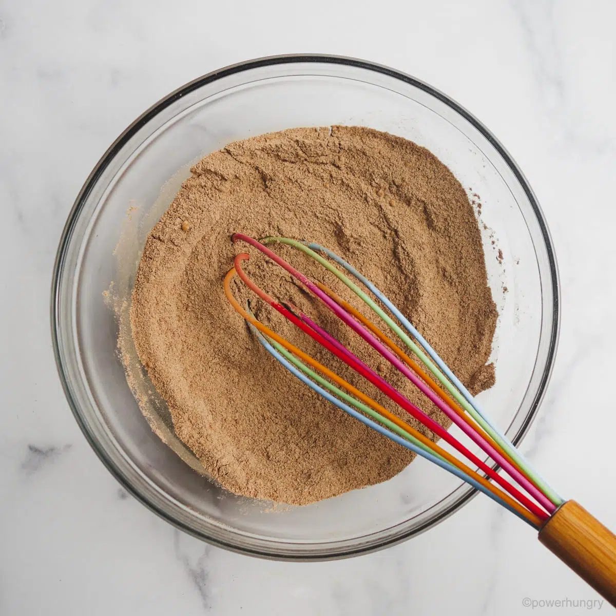 Dry chocolate buckwheat cookie ingredients in a glass bowl, whisked with a rainbow whisk