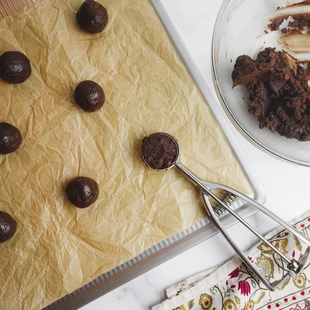 Chocolate buckwheat cookie dough portioned onto a parchment lined baking sheet