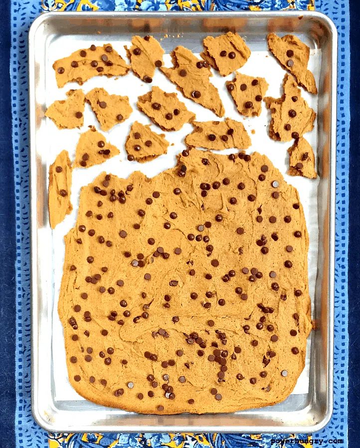 baked vegan chocolate chip cookie brittle on a baking sheet, some of it broken into pieces