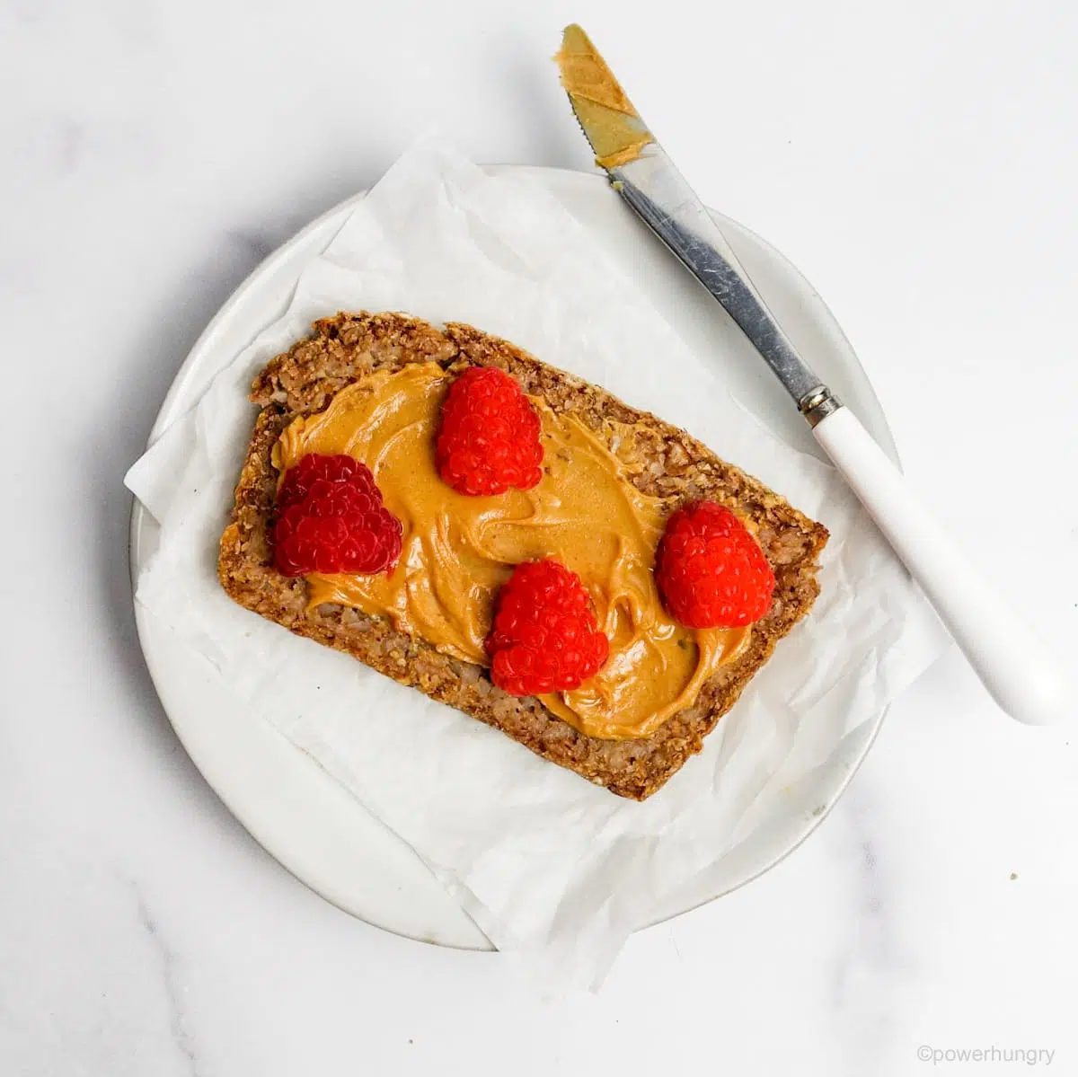 slice of bread topped with sunflower seed butter and raspberries, all atop a white plate