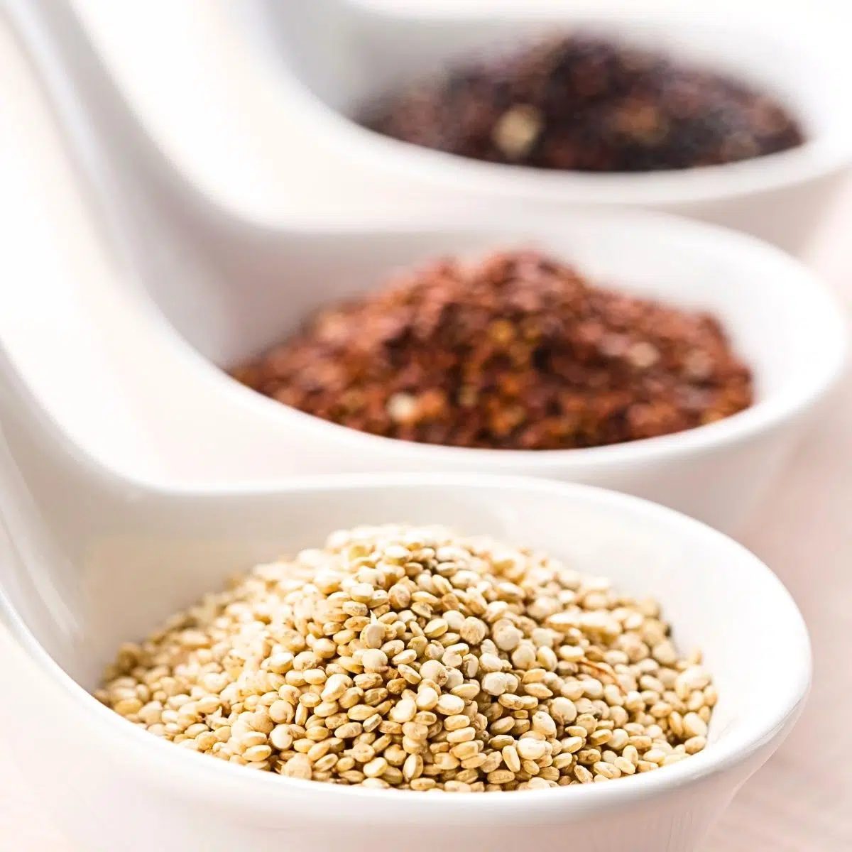 three white spoons filled with different colors of quinoa