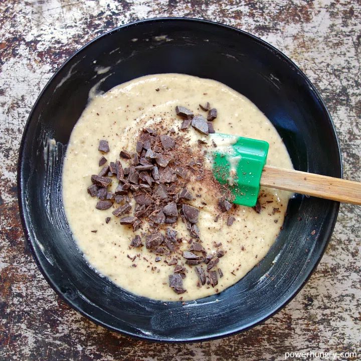 black potter bowl filled with cake batter, and chocolate chunks about to be stirred in
