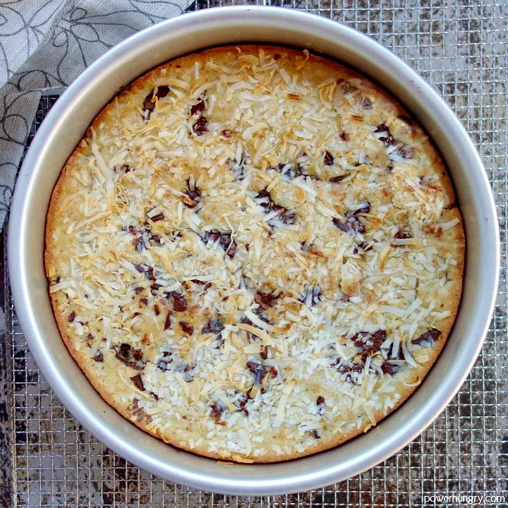 vegan coconut almond flour cake in a silver cake pan on top of a wire cooling rack