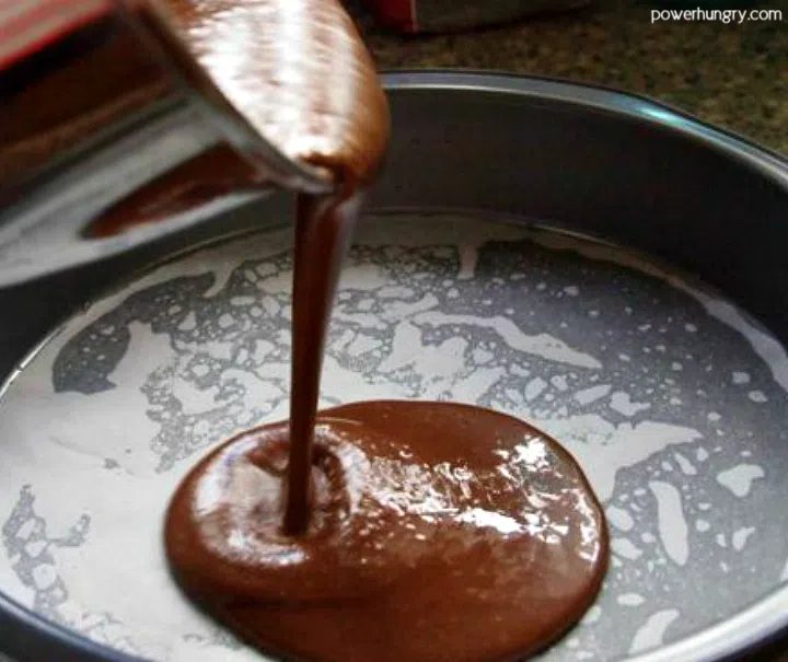 chocolate cake batter being poured into a metal cake tin