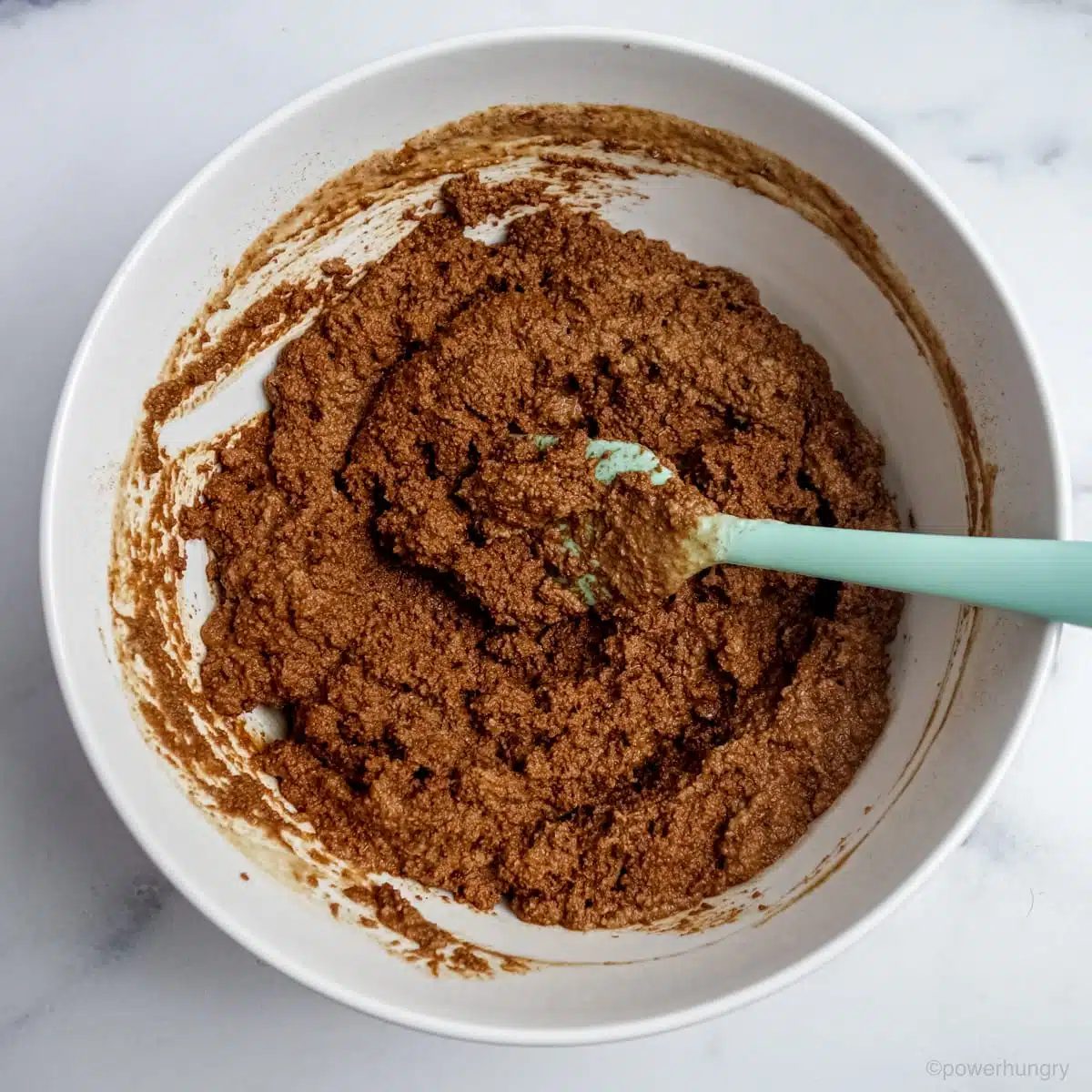 chocolate cupcake batter in a white bowl with a pale green spatula