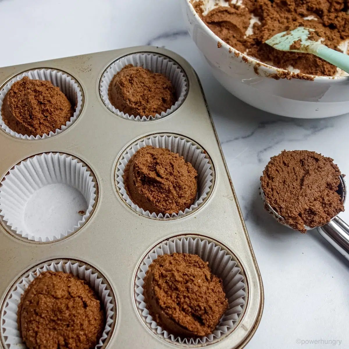 chocolate cupcake batter getting portioned into prepared muffin cups