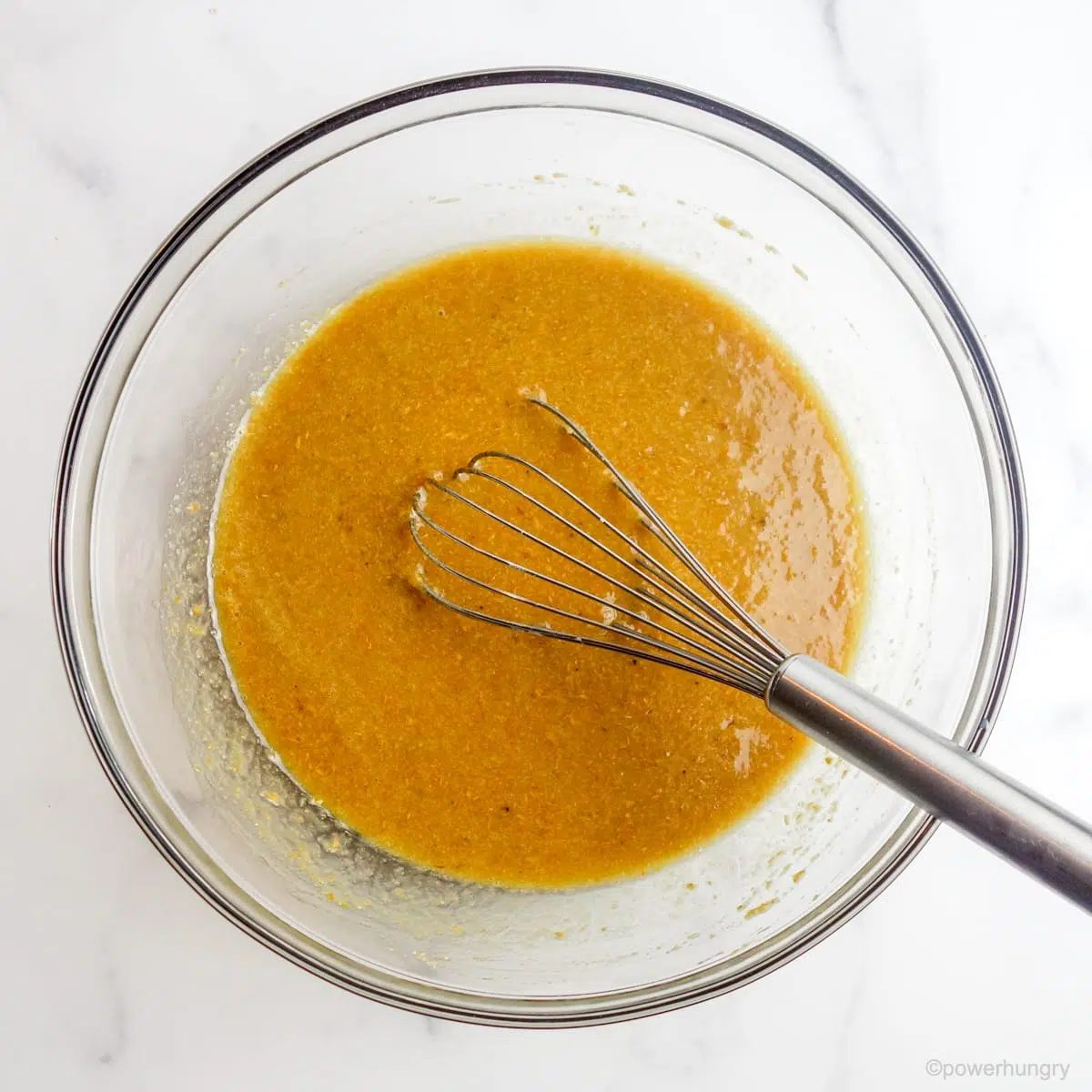 liquid batter ingredients in a glass bowl on a marble countertop
