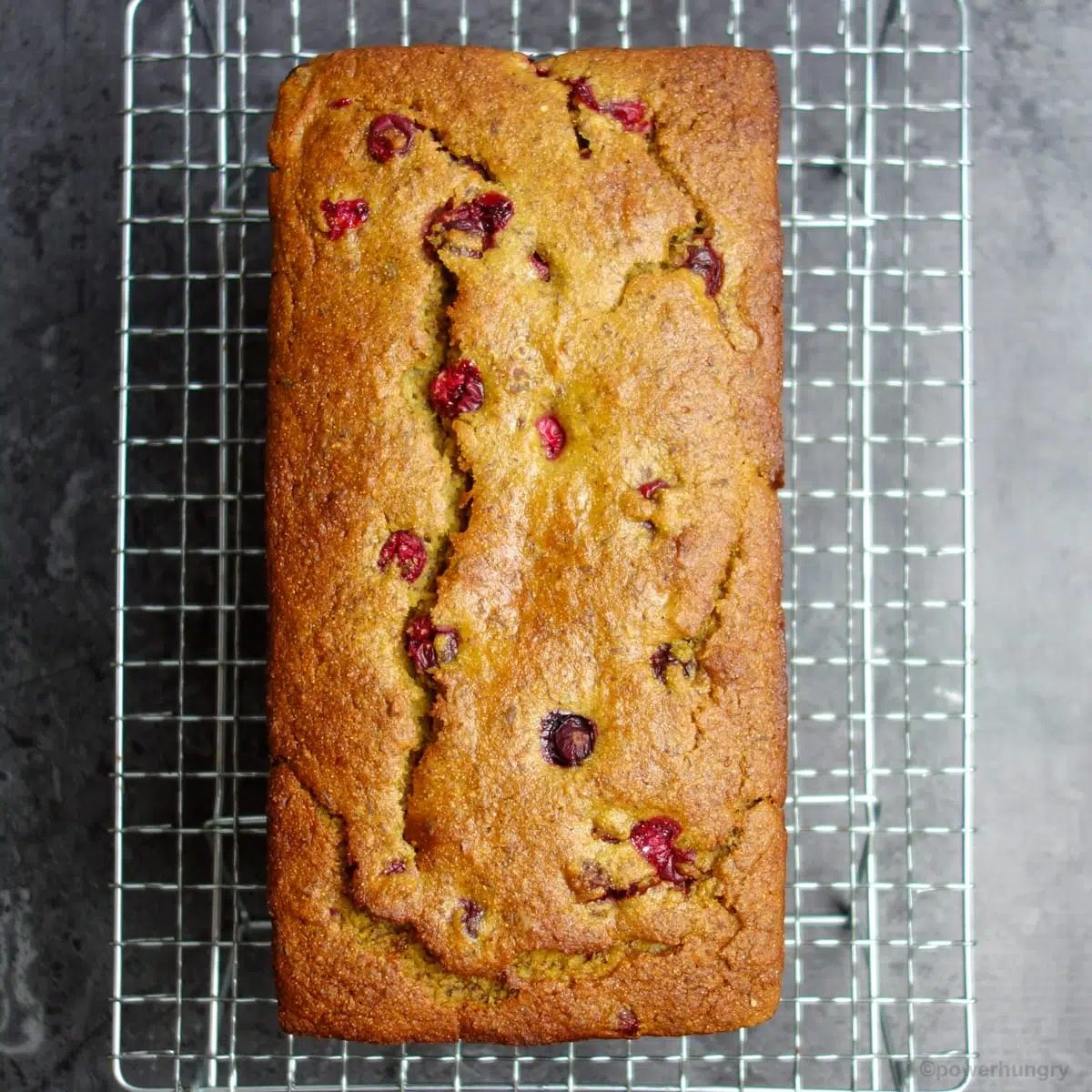 loaf of vegan chickpea flour cranberry orange bread ion a silver cooling rack