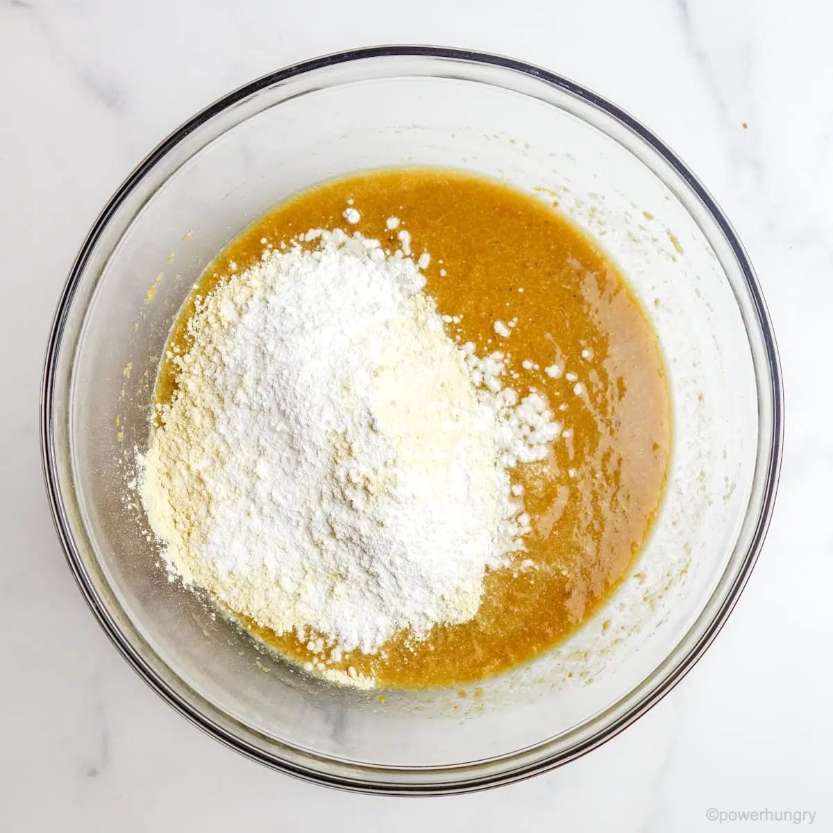 dry ingredients added to liquid ingredients in a glass bowl on a marble countertop
