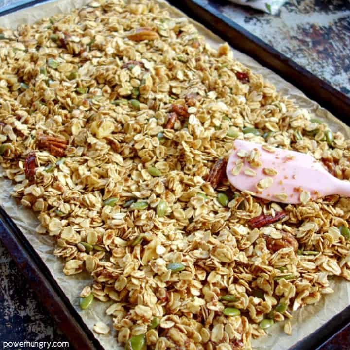 unbaked granola being spread on a baking dish with a pink spatula