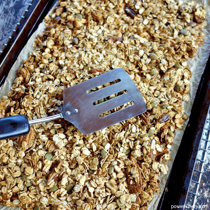 tamping down granola with a metal spatula after baking