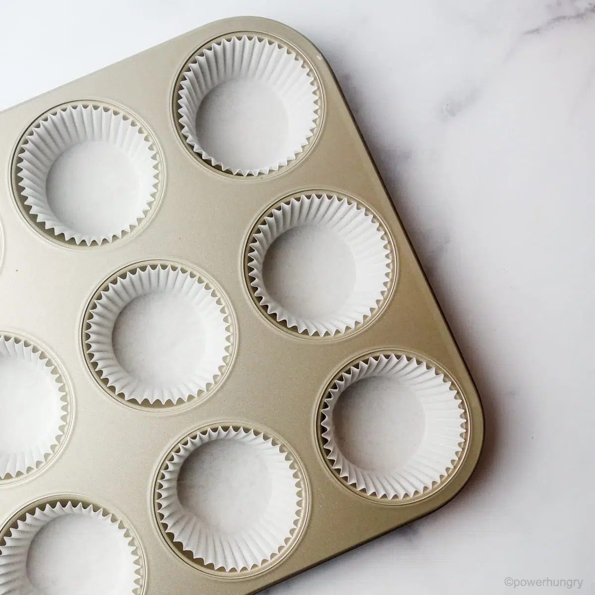 a silver muffin tin with eight of the cups lined with white paper liners