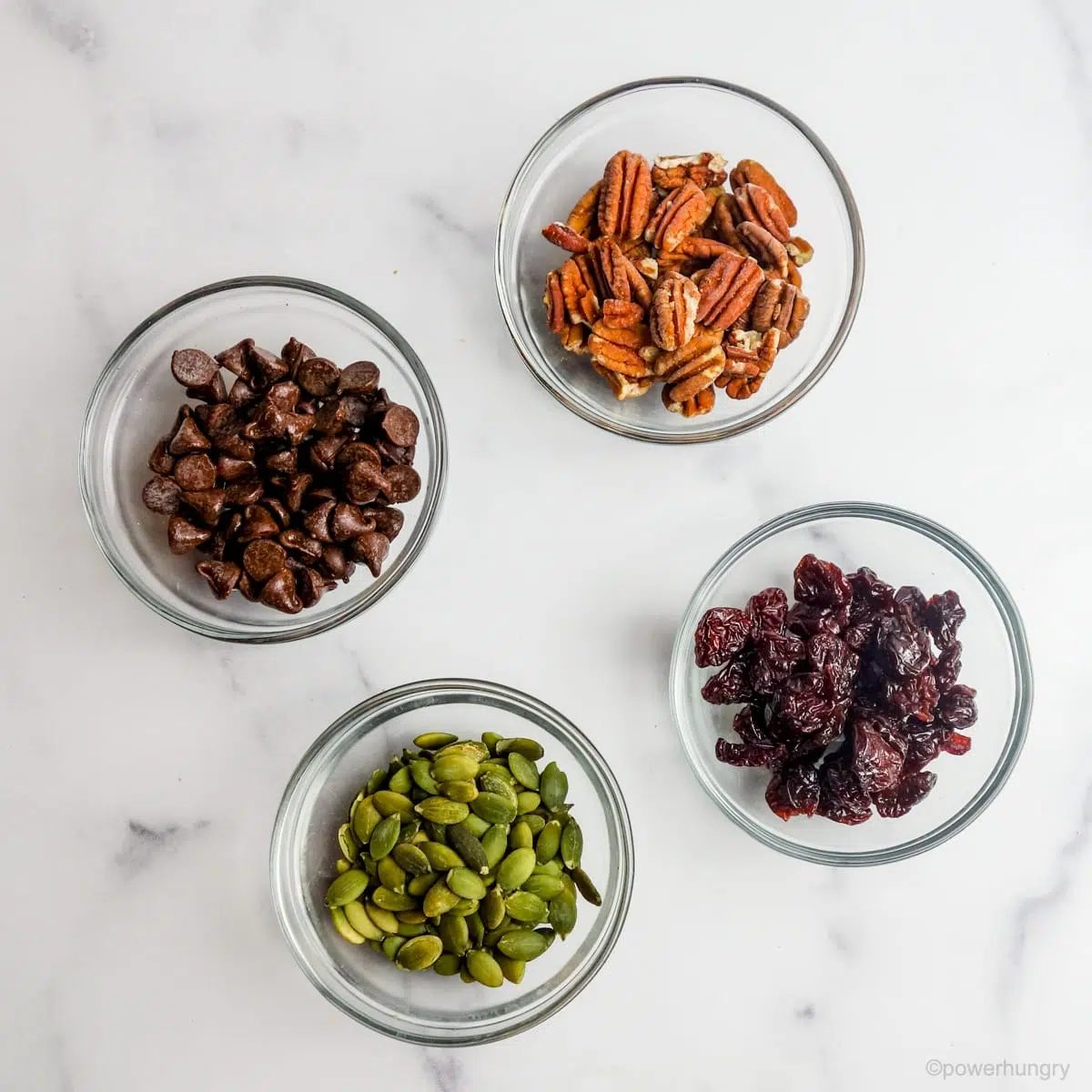 buckwheat muffin stir-in ingredients in small glass bowls on a marble countertop.