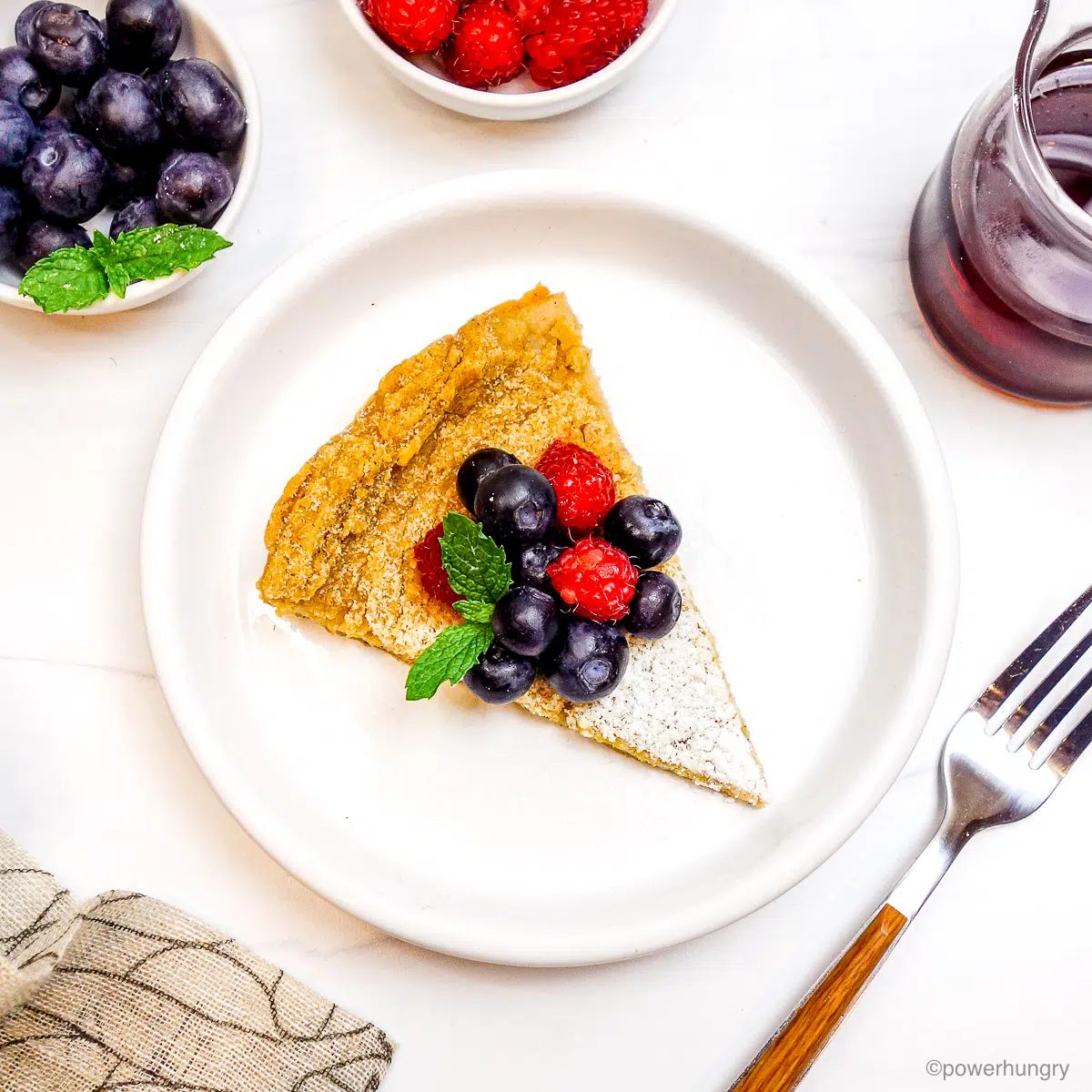 a wedge of vegan gluten-free Dutch baby on a white plate topped with powdered sugar and berries