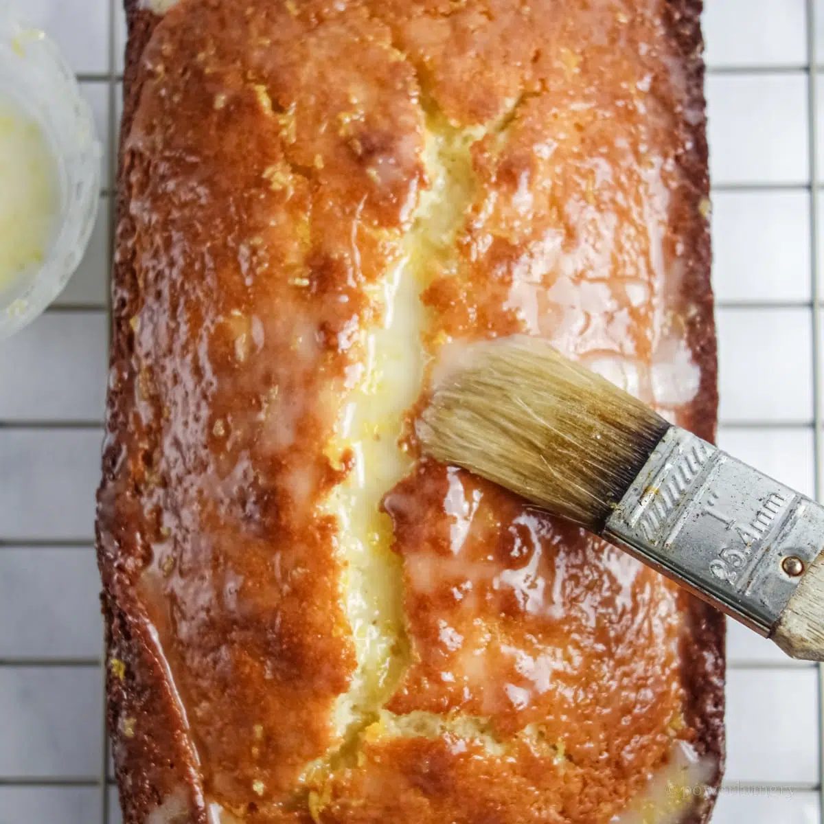overhead shot of vegan lemon loaf geting a lemon glaze brushed on top