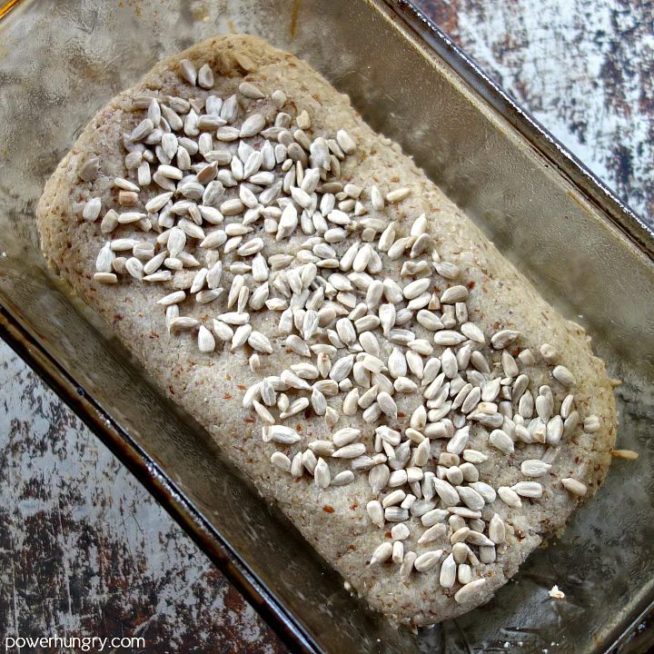 Sunflower seed bread dough in a glass loaf pan, topped with sunflower seeds