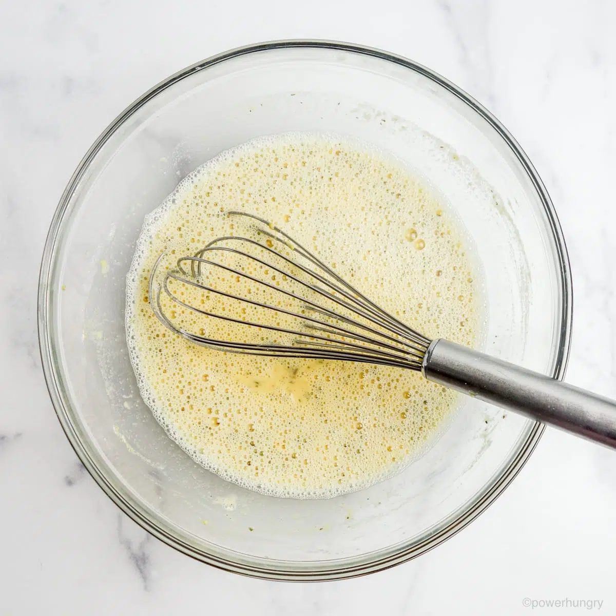 overhead shot of a glass bowl on a marble surface, filled with chickpea flour batter