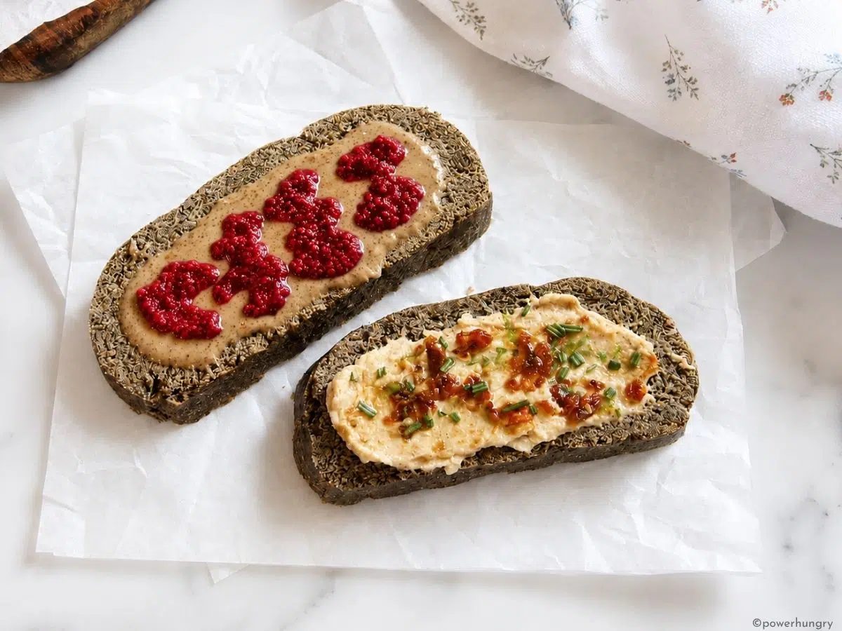 2 slices of oat fiber bread, one with almond butter and chia jam, the other with hummus and sun-dried tomatoes