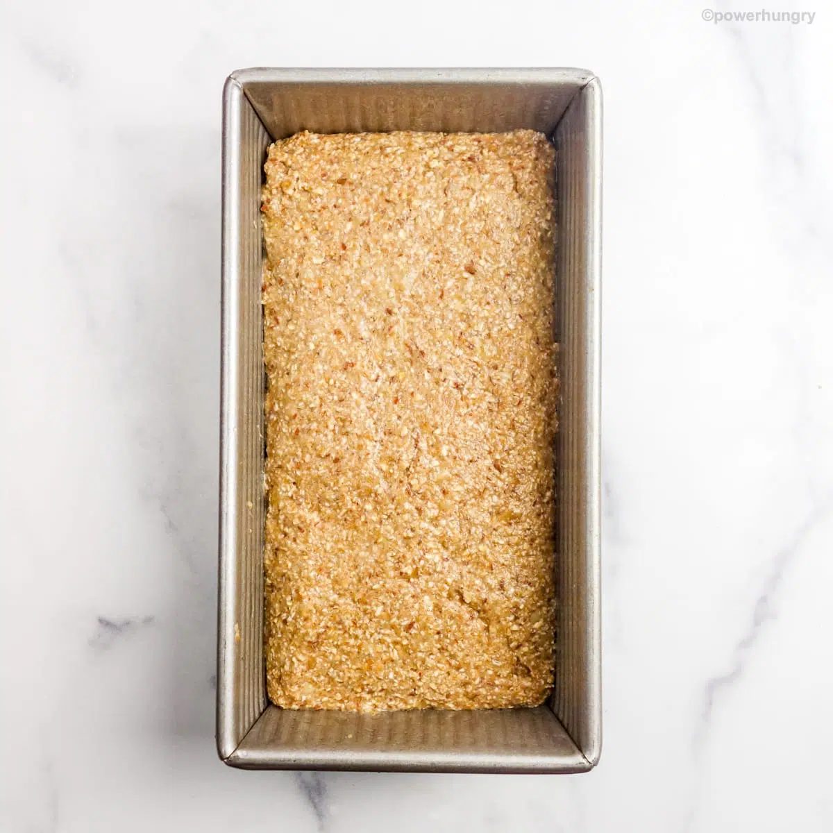 unbaked banana bread batter in a silver metallic loaf pan atop a marble board