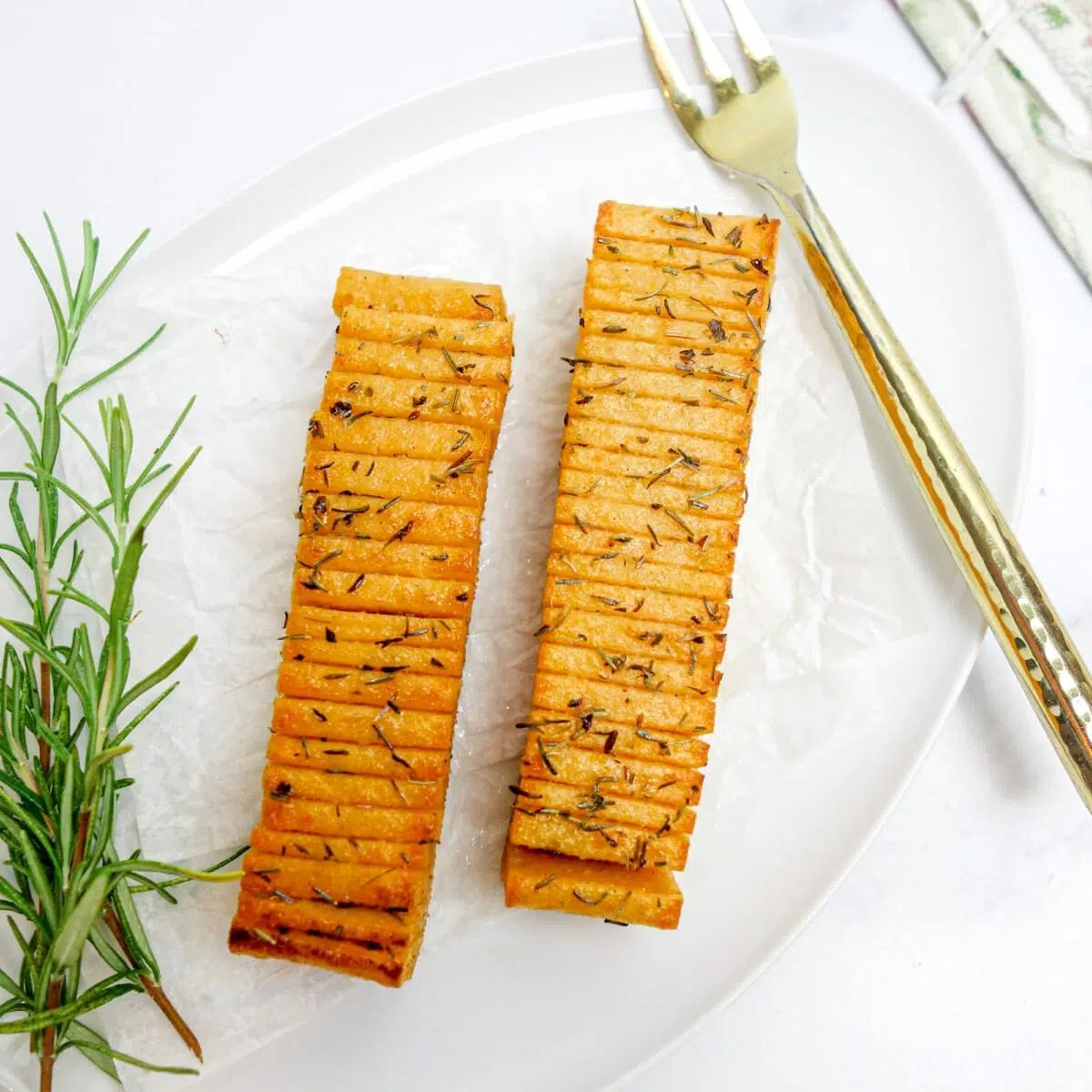 two fillets of vegan red lentil salmon on a white plate with a gold fork and sprigs of rosemary