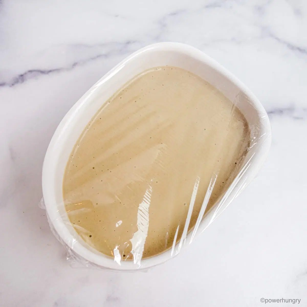 a white container filled with sunflower seed ice cream mixture and covered in plastic wrap