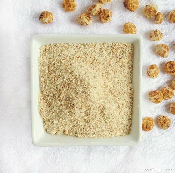 glass bowl full of tigernut flour, with some whole tigernuts alongside