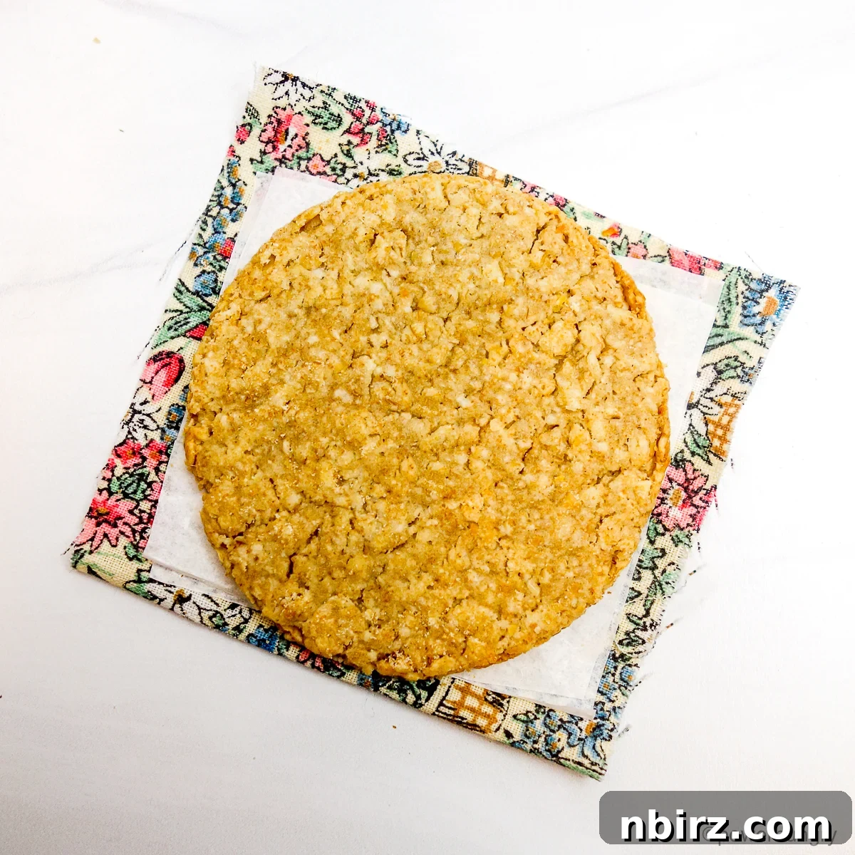 Wholesome Scottish Vegan Gluten Free Oatcakes 9 A single, perfectly round Scottish oatcake placed on a piece of parchment paper, resting on a charming floral napkin