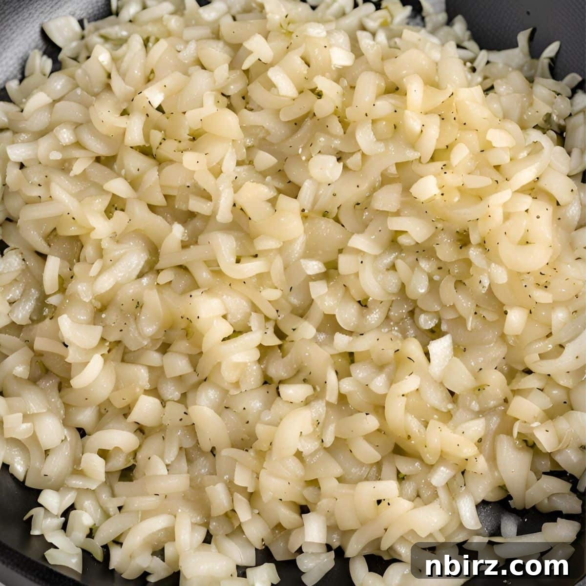 Finely chopped yellow onions sizzling and caramelizing in a hot skillet, becoming translucent and fragrant for the lentil taco meat.