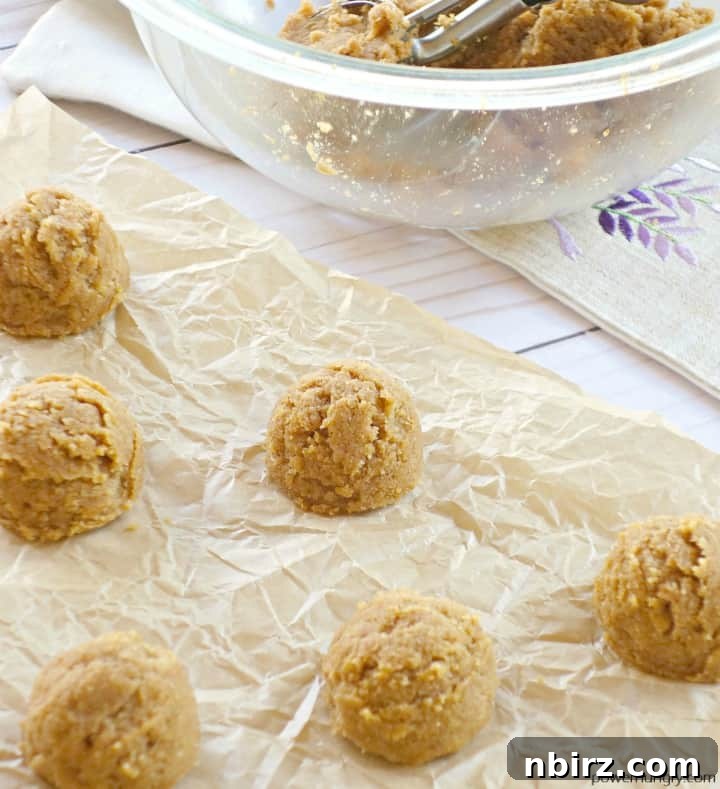 Wholesome Plant-Based Gluten-Free Pumpkin Almond Cookies 5 Neatly arranged mounds of unbaked vegan pumpkin almond cookie dough on a parchment-lined baking sheet, sprinkled with sugar.