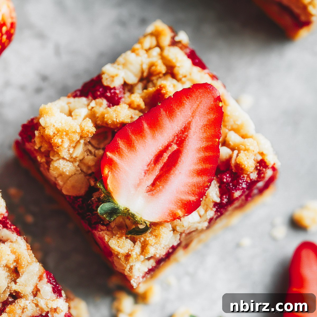Wholesome Gluten-Free Vegan Strawberry Oat Bars 5 A single healthy strawberry oatmeal bar, artfully topped with a fresh strawberry slice, on a textured background