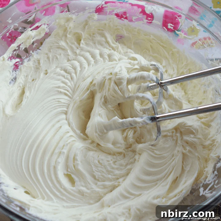 Silky Smooth Vegan Vanilla Buttercream Without Cornstarch 4 Glass bowl filled with creamy vegan vanilla frosting being beaten with electric beaters, creating a smooth texture.
