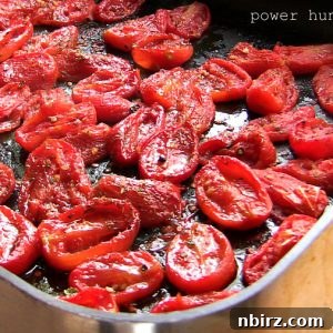 Caramelized Whole Canned Tomatoes 3 A close-up of golden-brown roasted whole canned tomatoes glistening with olive oil and specks of black pepper, arranged neatly in a large baking sheet.