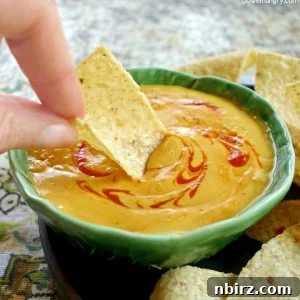 A bowl of vibrant orange chickpea flour queso with tortilla chips for dipping.