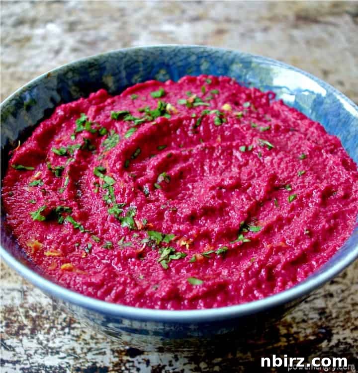 Velvety Beet and Toasted Pepita Dip 3 An elegant blue pottery dish brimming with vibrant beet and toasted pepita dip, beautifully garnished with fresh green herbs and bright lemon zest for an inviting presentation.