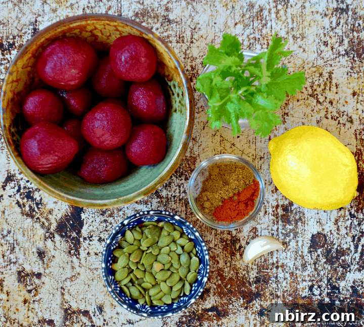 Velvety Beet and Toasted Pepita Dip 4 An artistic overhead view of all ingredients for the beet and pepita dip thoughtfully arranged on a textured surface, including canned beets, vibrant green pepitas, various spices, a fresh lemon, and a clove of garlic.