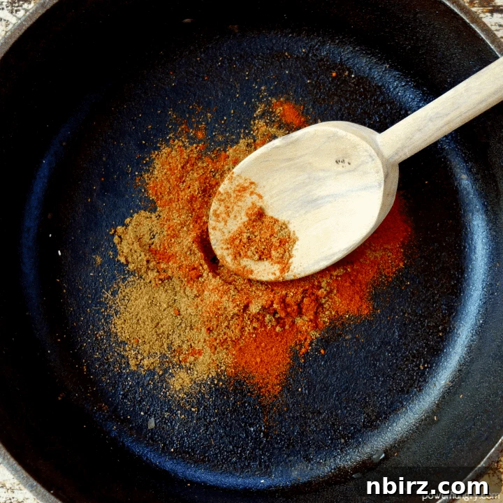 Velvety Beet and Toasted Pepita Dip 6 Close-up view of vibrant red smoked paprika and earthy brown cumin being gently stirred in a cast iron skillet with a wooden spoon, releasing their enticing aromas.