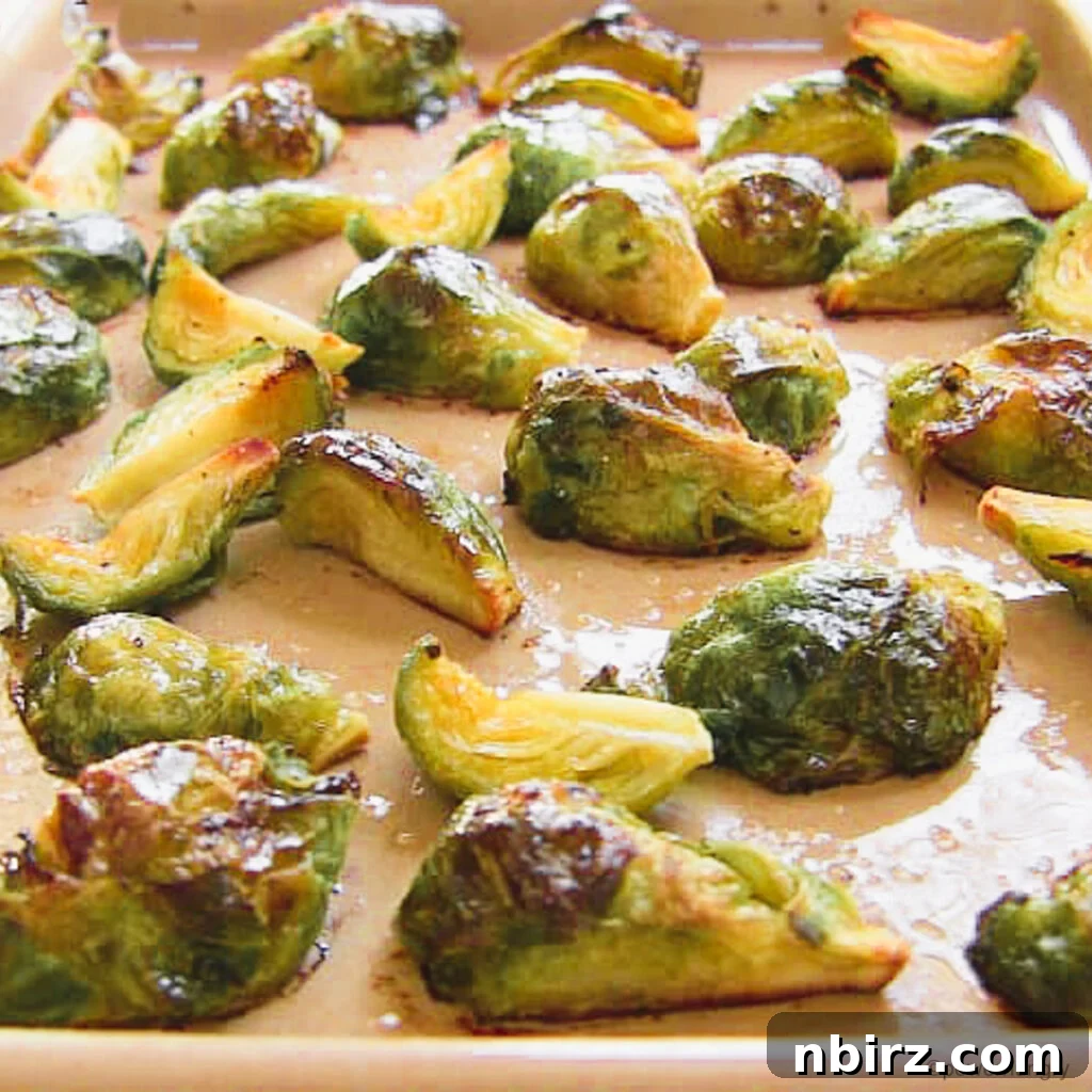 Protein-Packed Oil-Free Brussels Sprouts Quinoa Pomegranate Salad 3 Close-up shot of perfectly roasted Brussels sprouts on an earthenware baking sheet, showing their browned and tender appearance.