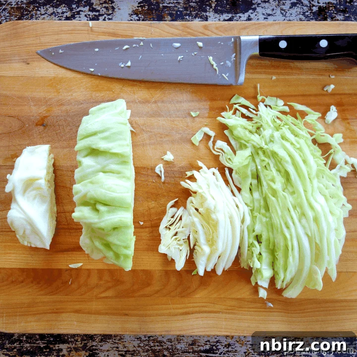 Caboodles: One-Ingredient Vegan Keto Steamed Cabbage Noodles 6 Thin strips of green cabbage are meticulously cut on a wooden cutting board, illustrating the process of creating homemade cabbage noodles, ready for steaming.