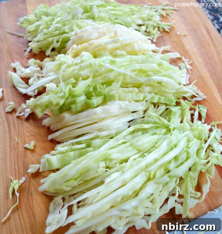 Caboodles: One-Ingredient Vegan Keto Steamed Cabbage Noodles 7 A pile of thinly sliced green cabbage strips rests on a rustic wooden cutting board, perfectly prepared to be transformed into healthy cabbage noodles.