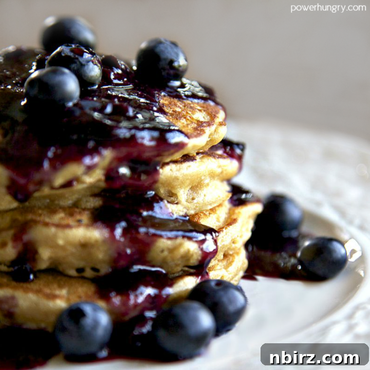 A stack of golden-brown chickpea flour pancakes on a white plate, generously topped with fresh blueberries, inviting you to take a bite.