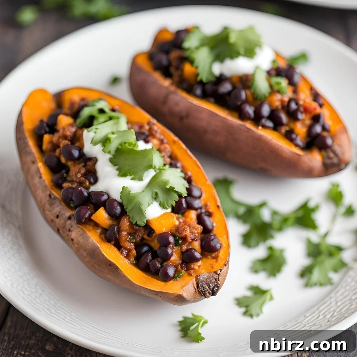 4-Ingredient Black Bean Chili Stuffed Sweet Potatoes 2 black bean chili stuffed sweet potatoes on a white plate