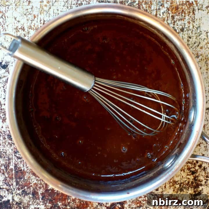 Heated chocolate mixture simmering gently in a stainless steel saucepan, ready for the oats to be added.