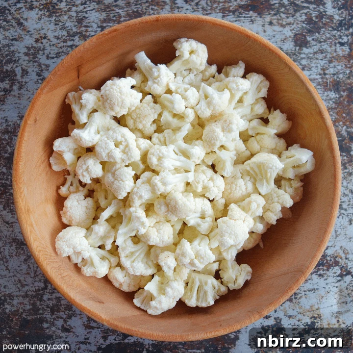 Wooden bowl overflowing with freshly cut cauliflower florets, ready for seasoning and baking.