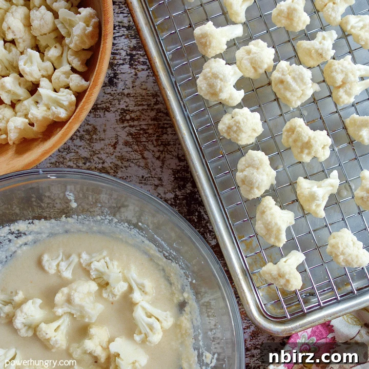 Hands tossing cauliflower florets in almond flour batter within a glass bowl, preparing them for baking.