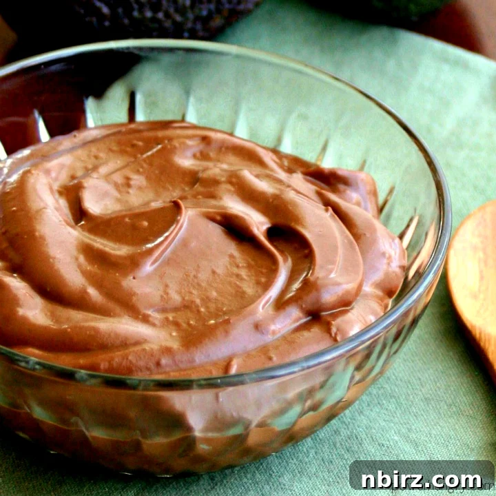 Healthy vegan chocolate avocado pudding in a glass bowl atop a green napkin, garnished with fresh berries.